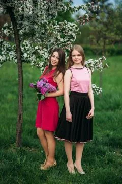 Two sisters walking outside in spring park. They hold a bouqet of lilac and Stock Photos