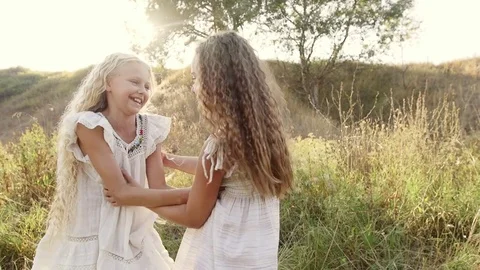 Two sisters in white dresses in the garden at sunset. The girls hug and laugh Stock Footage 80348012