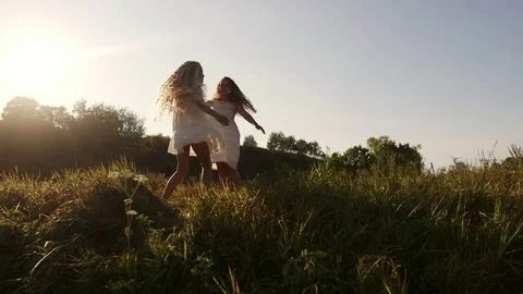 Two sisters in white dresses in the garden at sunset. The girls hug and laugh Stock Footage 80348608