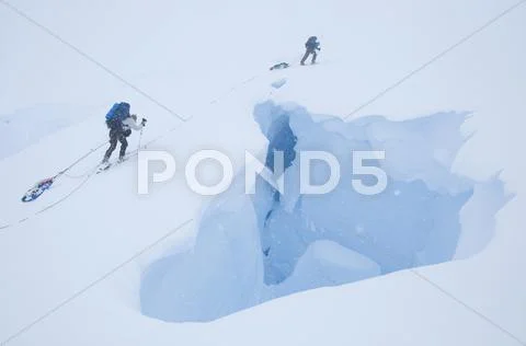 Two skiers on an extended ski traverse cross a gaping crevasse in the remote Stock Photos
