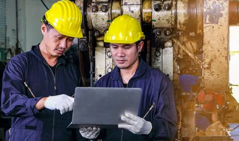 Two skilled Asian workers, dressed in helmet uniforms, were using a computer. Foto stock