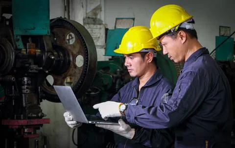 Two skilled Asian workers, dressed in helmet uniforms, were using a computer. Stock Photos