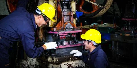 Two skilled Asian workers, dressed in helmet uniforms, are discussing machine Stock Photos