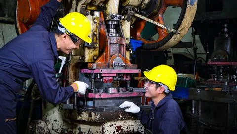 Two skilled Asian workers, dressed in helmet uniforms, are discussing machine Foto stock