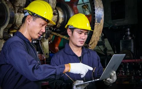 Two skilled Asian workers, dressed in helmet uniforms, were using a computer. Stock Photos