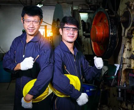 Two skilled Asian workers, dressed in helmet uniforms, are discussing machine Stock Photos