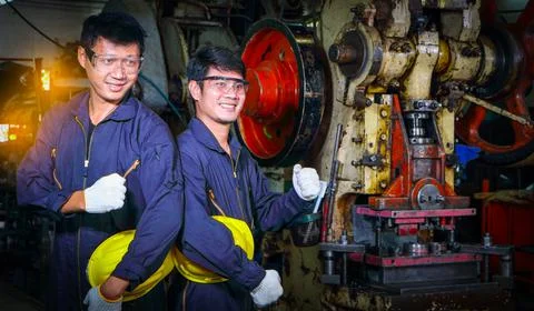 Two skilled Asian workers, dressed in helmet uniforms, are discussing machine Foto stock