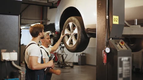 Two skillful father and son mechanics using tablet in auto repair shop. Car Stock Footage 243744478