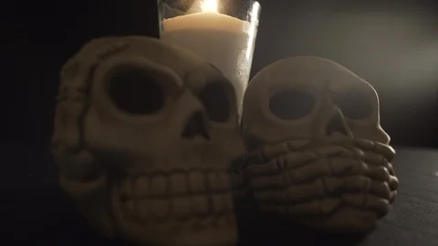 Two skulls infront of candle light up on a black background Stock Footage 96688236
