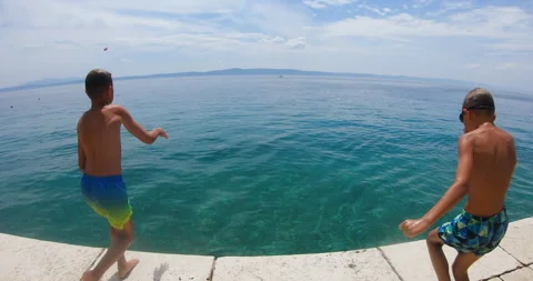 Two slender guys jumping from pier into clear sea during summer holiday on blue Stock Footage 194269637