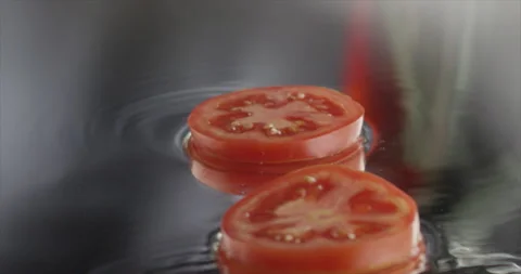 Two slice of tomato spinning falling on a mirror surface Stock Footage 198345990