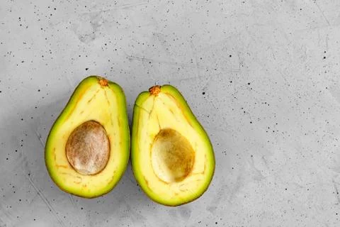 Two slices of avocado cut in half, one slice with core on gray concrete backg Foto stock