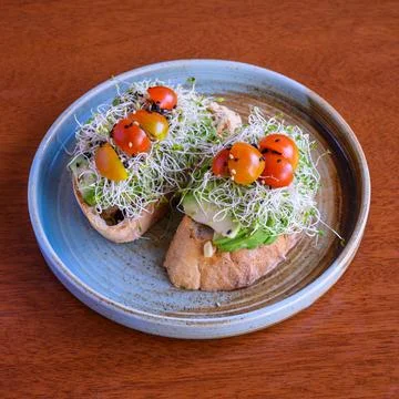Two slices of bread with avocado and alfalfa sprouts on blue plate Stock Photos