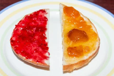 Two slices of bread with strawberry jam and apricot preserves on a plate Stock Photos
