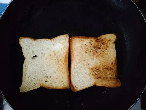 Two Slices of Bread Toasting in a Black Pan. Stock Photos