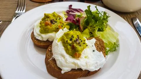 Two slices of dark bread with poached eggs on a white plate. 库存照片