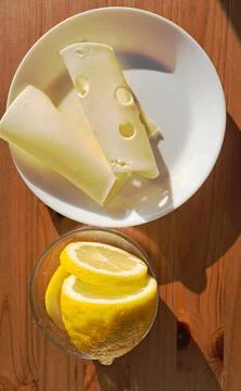 Two slices of hard cheese placed  on a wooden table next to a cut lemon . Stock Photos