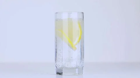 Two slices of lemon fall into a transparent glass of water Stock Footage 229503619