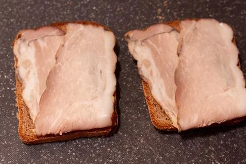 Two slices of rye bread with smoked pork belly fat on dark background Фото