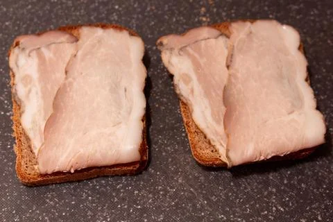 Two slices of rye bread with thin smoked pork belly bacon on dark grey 库存照片