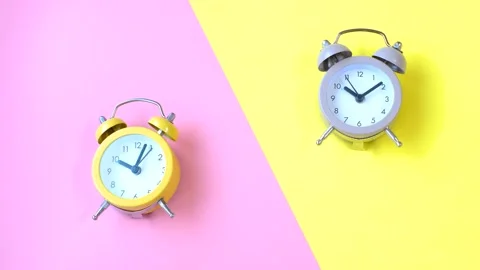Two small alarm clocks on pink and yellow background close-up top view. Stock Footage 294492549