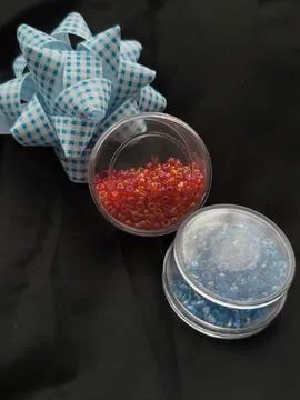 Two small boxes with blue and red beads near a bow on a black background Stock Photos