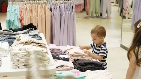 Two small children in a store are choosing things for themselves in a clothing Stock Footage 202324422