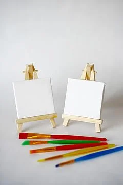Two small easels and multicolored brushes for painting on a light background. Stock Photos