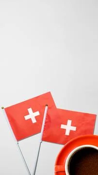 Two small flags of Switzerland next to a cup of black coffee on a light gra.. 写真素材