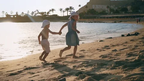Two small happy children run holding hands along the beach near the sea at Stock Footage 104185764