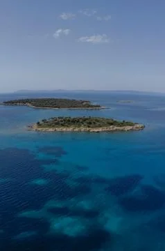 Two small islands surrounded with blue sea water with mountains in background Stock Photos