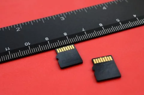 Two small micro SD memory cards lie on a red background next to a black ruler Stock Photos