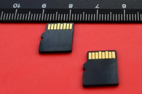 Two small micro SD memory cards lie on a red background next to a black ruler Stock Photos