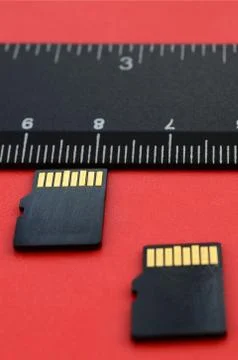Two small micro SD memory cards lie on a red background next to a black ruler Stock Photos