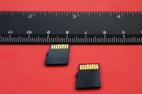 Two small micro SD memory cards lie on a red background next to a black ruler Stock Photos