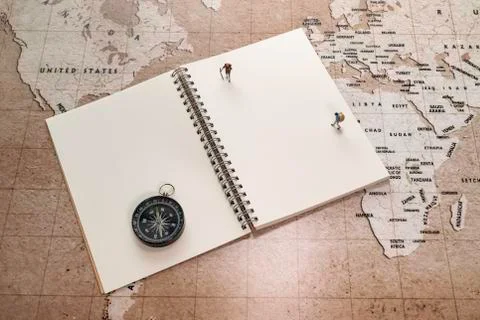 Two small miniatures on white notebook with compass on world map Stock Photos