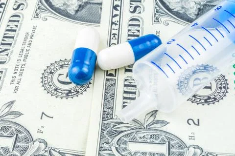 Two small pills and one injection are laying on dollar banknotes Stock Photos