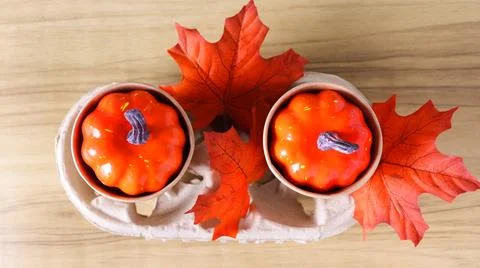 Two small pumpkins placed on a wooden table with colorful leaves in an autumn Stock Photos