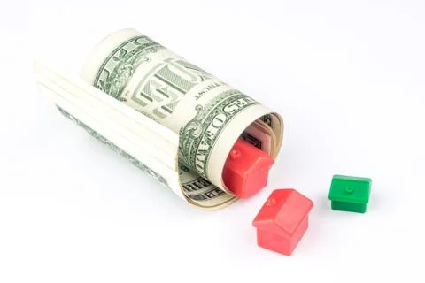 Two small red and one green houses are coming out from rolled bunch of dollar Stock Photos