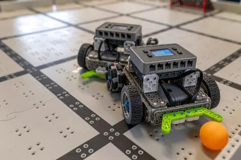 Two small robots are positioned on a grid-patterned floor, ready for a task i 스톡 사진