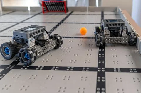 Two small robots are positioned on a grid-patterned floor, ready for a task i Stock Photos