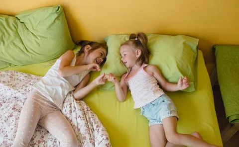 Two small smiling cute sisters are playing in bed, top view. happy childhood Stock Photos