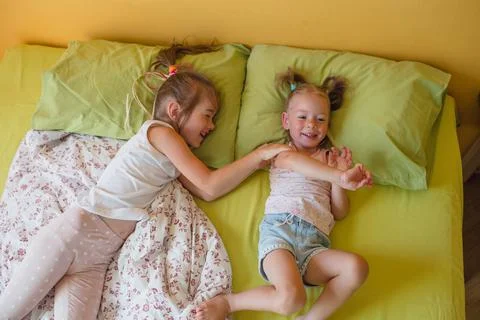 Two small smiling cute sisters are playing in bed, top view. happy childhood Stock Photos