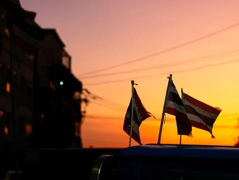 Two Small Thai National Flags on Car Roof Waving in Wind Against Orange Sun.. Fotos Stock