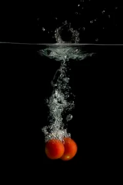Two small tomatoes falls under water with splash Stock Photos