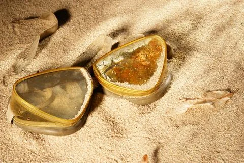 Two small, triangular, gold-colored containers are laying on the sand Stock Photos
