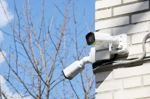 Two small white CCTV cameras on the corner of the facade of a multi-storey br Stock Photos