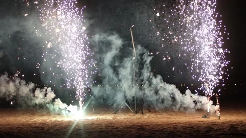 Two small white firework burning and exploding - spreads sparkles on the beach Stock Footage 133026414