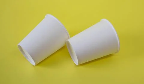 Two small white paper cups on a yellow background Stock Photos