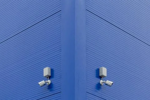 Two small white security cameras on blue steel building corner Stock Photos